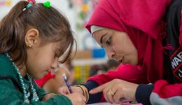 War Child medewerker in Jordanië met War Child-logo helpt kind lezen_War Child Jordanië_180424