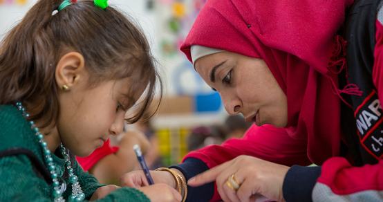 War Child medewerker in Jordanië met War Child-logo helpt kind lezen_War Child Jordanië_180424