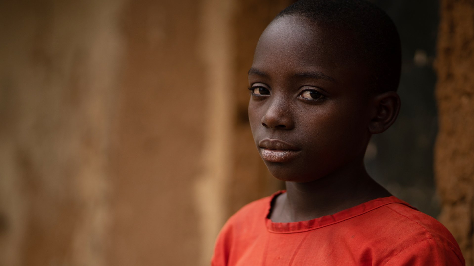 Meisje Ariane in Oeganda - kijkt camera in, draagt rode jurk - War Child Doorbreek het zwijgen