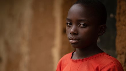 Meisje Ariane in Oeganda - kijkt camera in, draagt rode jurk - War Child Doorbreek het zwijgen