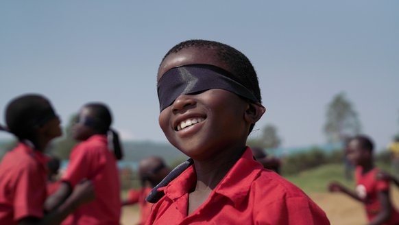 Kind speelt geblinddoekt tijdens TeamUp activiteiten War Child in Oeganda