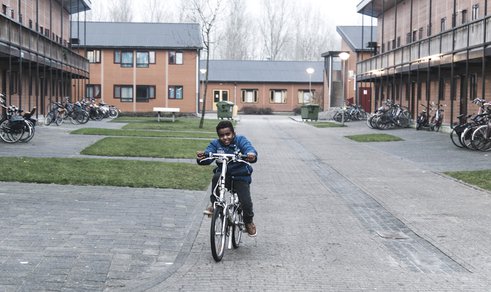 Een jongen fietst over het terrein van azc Almere credits Stichting de Vrolijkheid-Petra Katanic.jpg