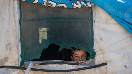 Glurend uit het raam van de tent in Lebanon zit een kind in lockdown vanwege corona