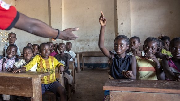 Meisje steekt haar hand op in de klas op school waar zij onderwijs krijgt dankzij War Child