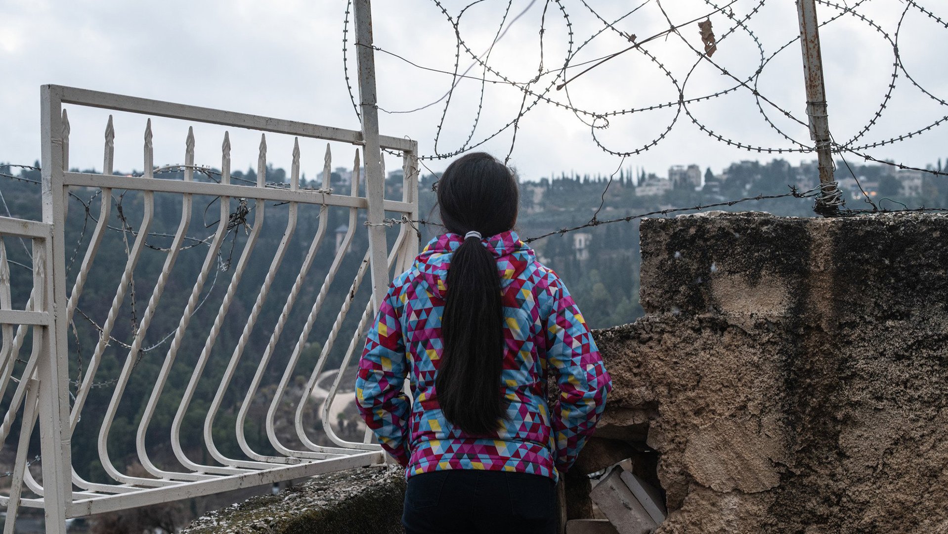 Girl facing away in front of barbed wire in OPT near War Child safe space