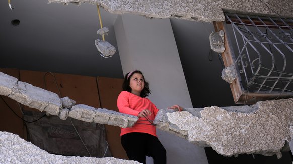 Palestinian girl, Sara, standing in her destroyed house