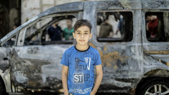 Boy standing in front of burnt out vehicle